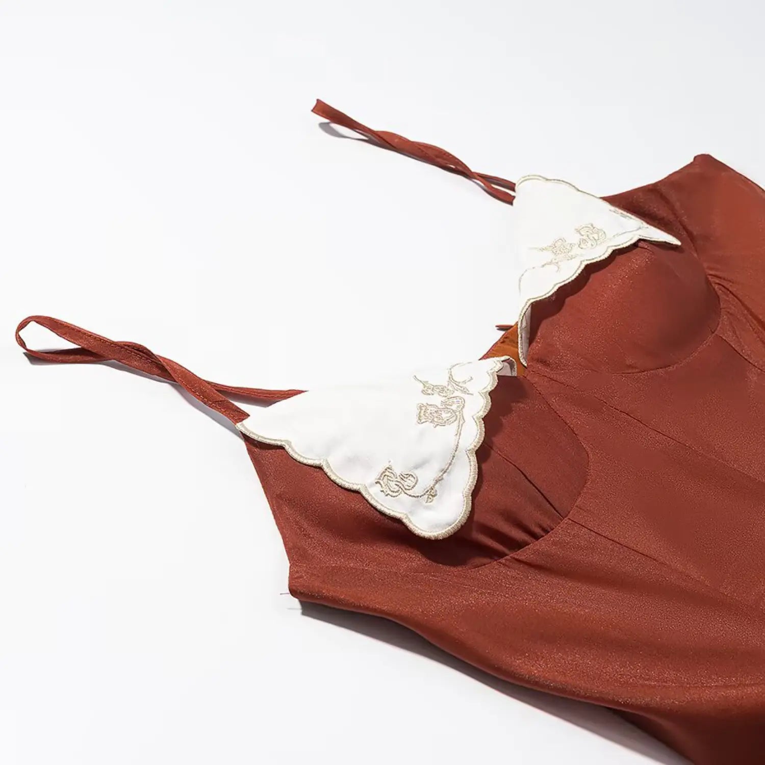 Close‑up shot rust orange camisole dress focusing on white scalloped collar with golden floral embroidery