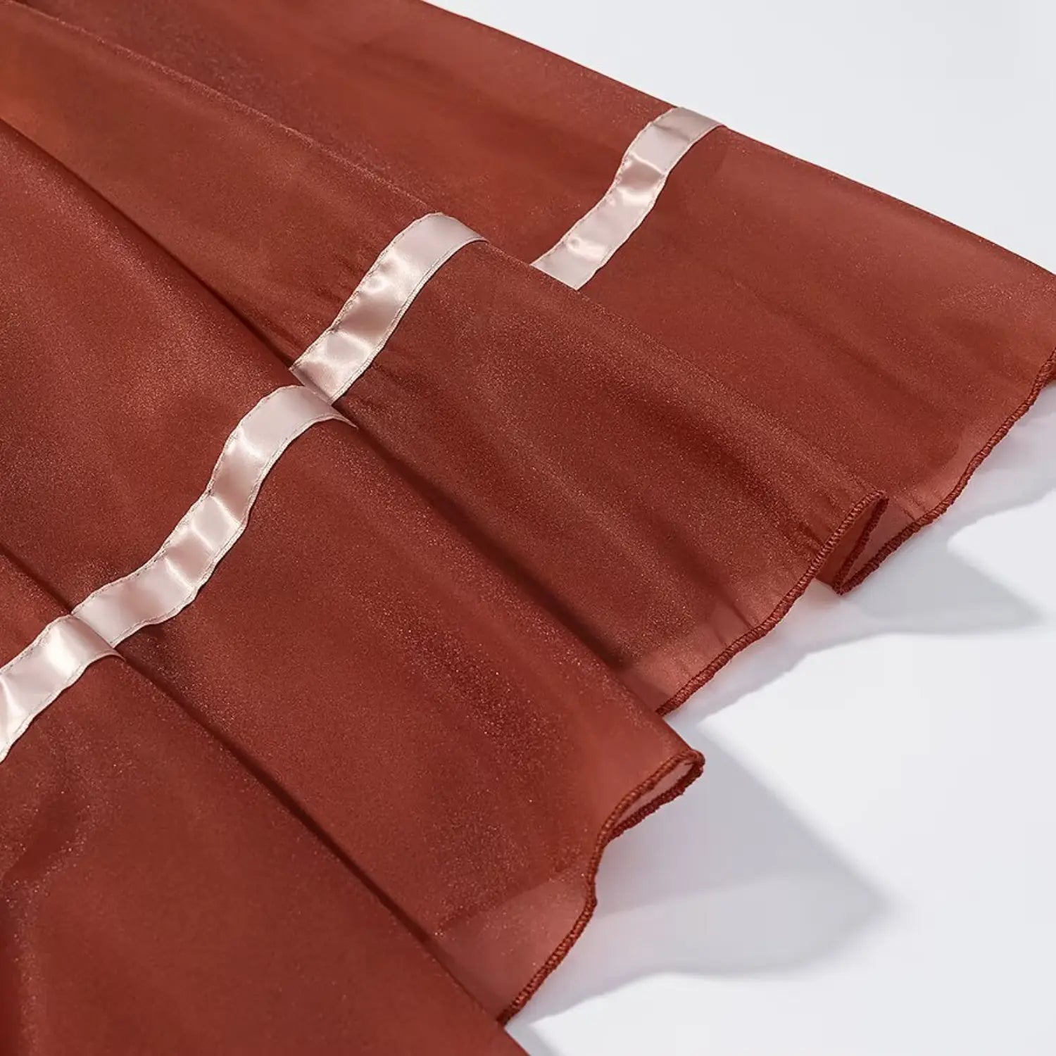 Close‑up view of skirt hem with white satin ribbon trim on sheer rust orange chiffon fabric