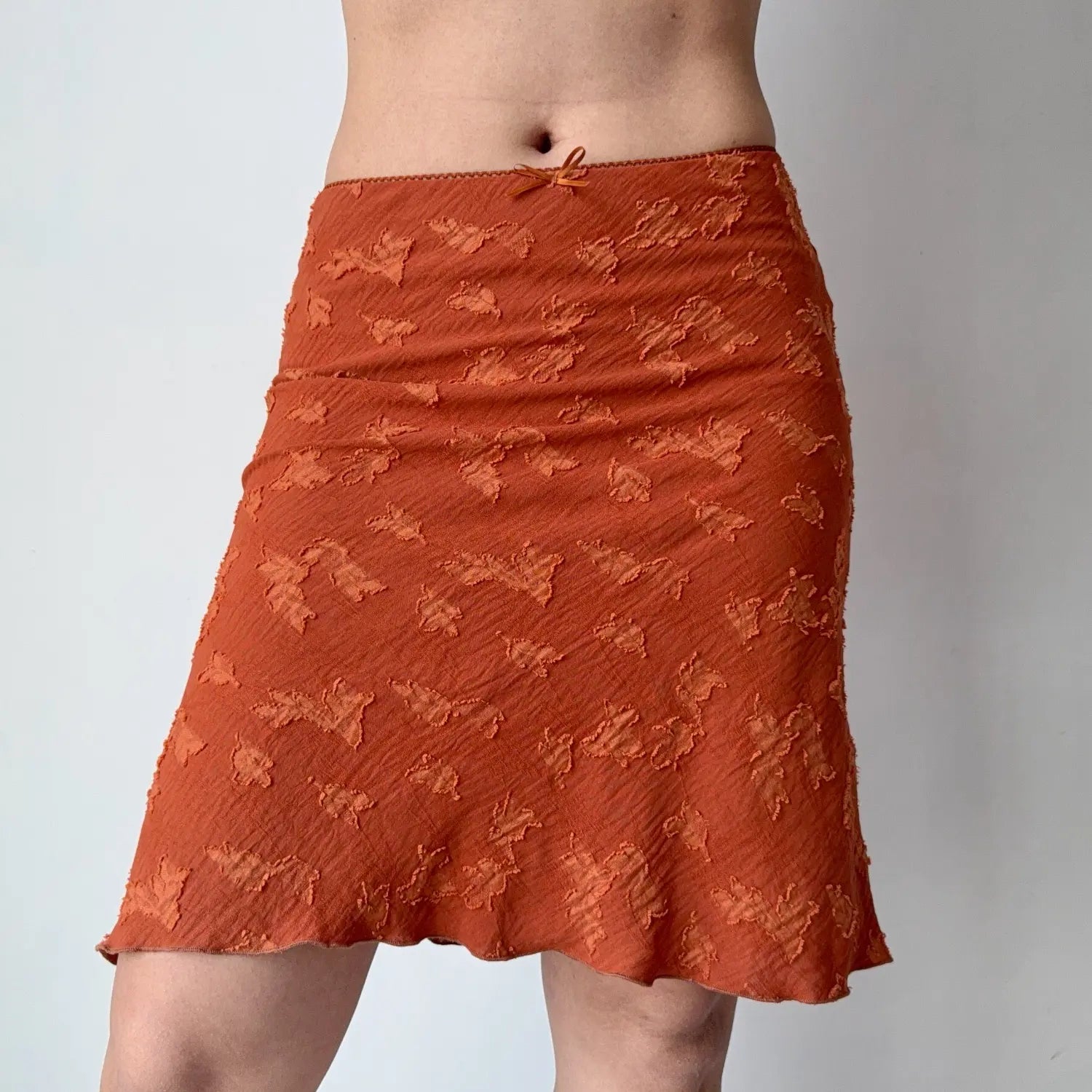 Front lifestyle shot on model of rust orange textured floral skirt, subtle side ruching, mid-length flared silhouette
