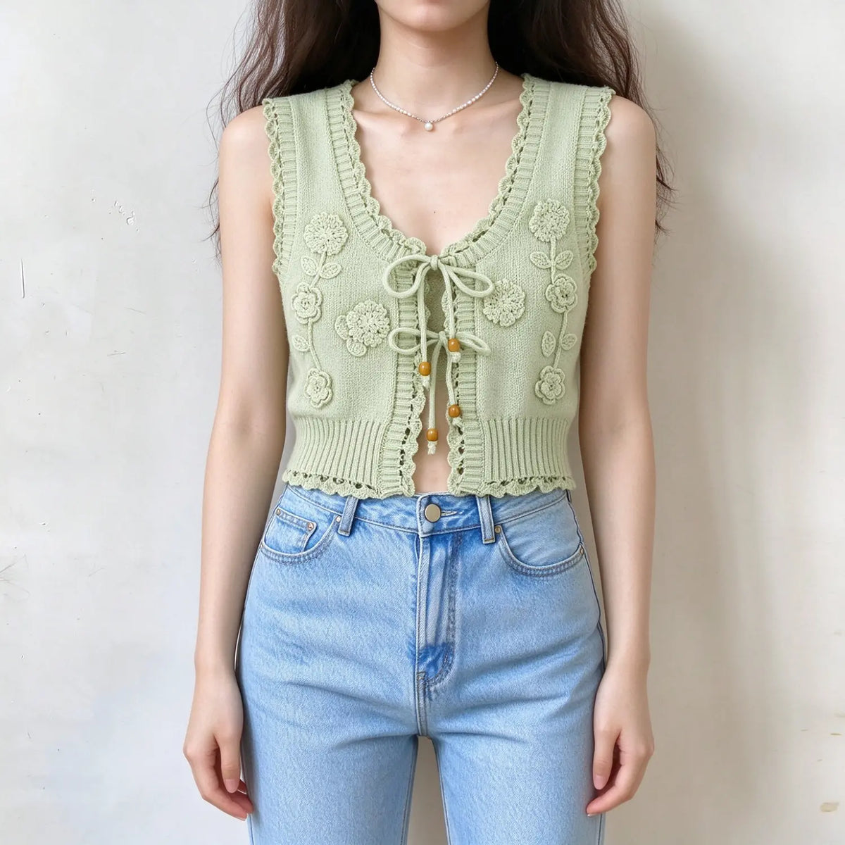 Model wearing sage green crochet flower tie front knit vest with jeans, front view
