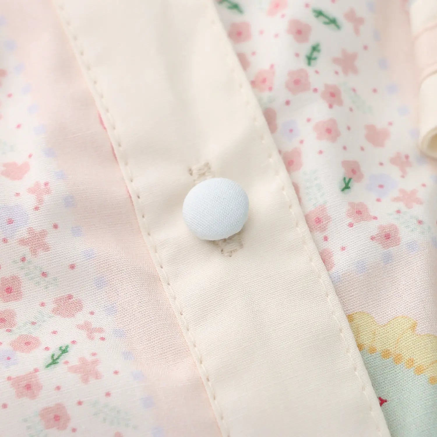 Cartoon print sailor collar blouse front fabric covered button macro close-up, cream self-fabric wrapped round buttons double secure stitching neat double binding placket delicate sewing craft shot