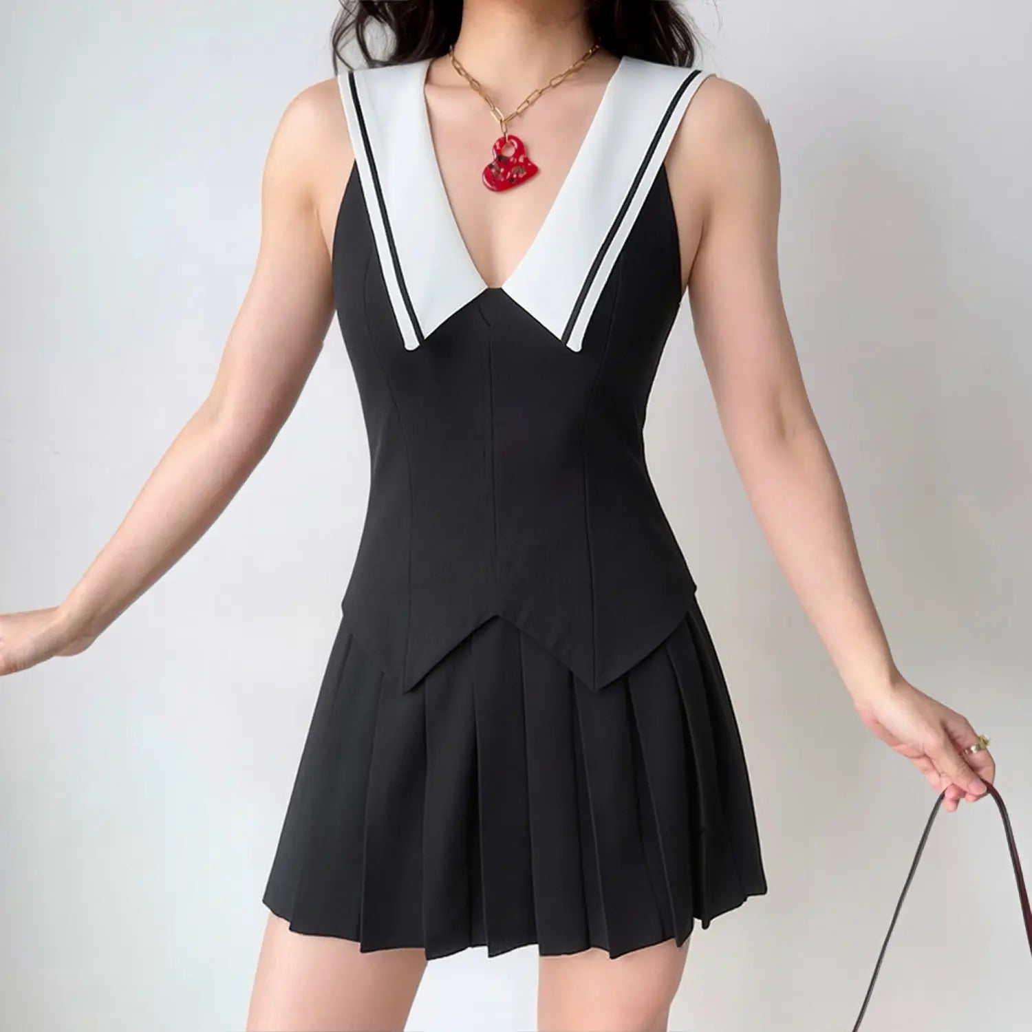 Model daily outfit shot, black sleeveless sailor mini dress, deep V white piped lapel, fitted pointed waist, bouncy box pleat skirt, styled with vintage red pendant necklace, youthful preppy campus style