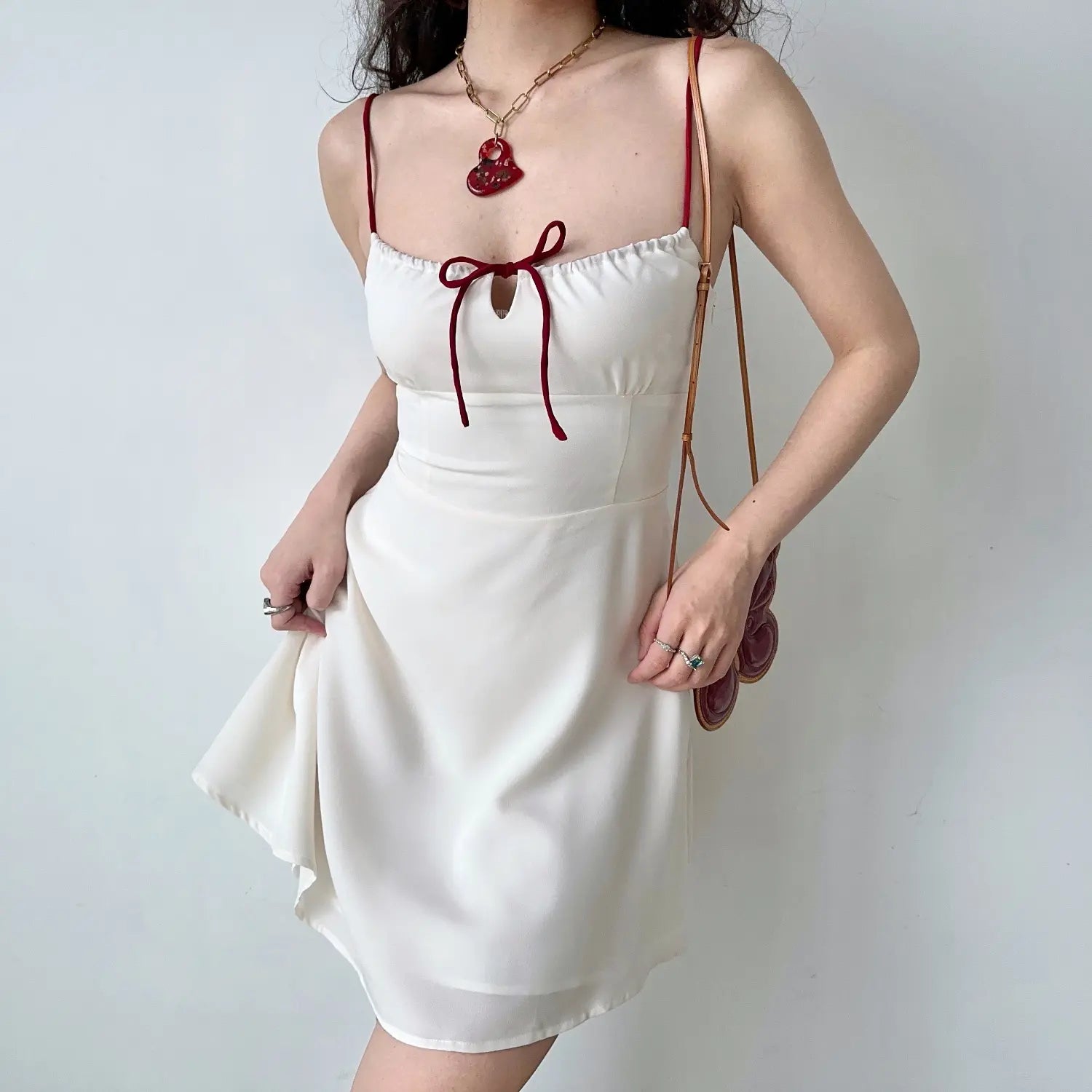 Close up flowy skirt detail white satin mini dress, burgundy spaghetti straps, front chest ribbon tie keyhole cutout, slim fitted waist