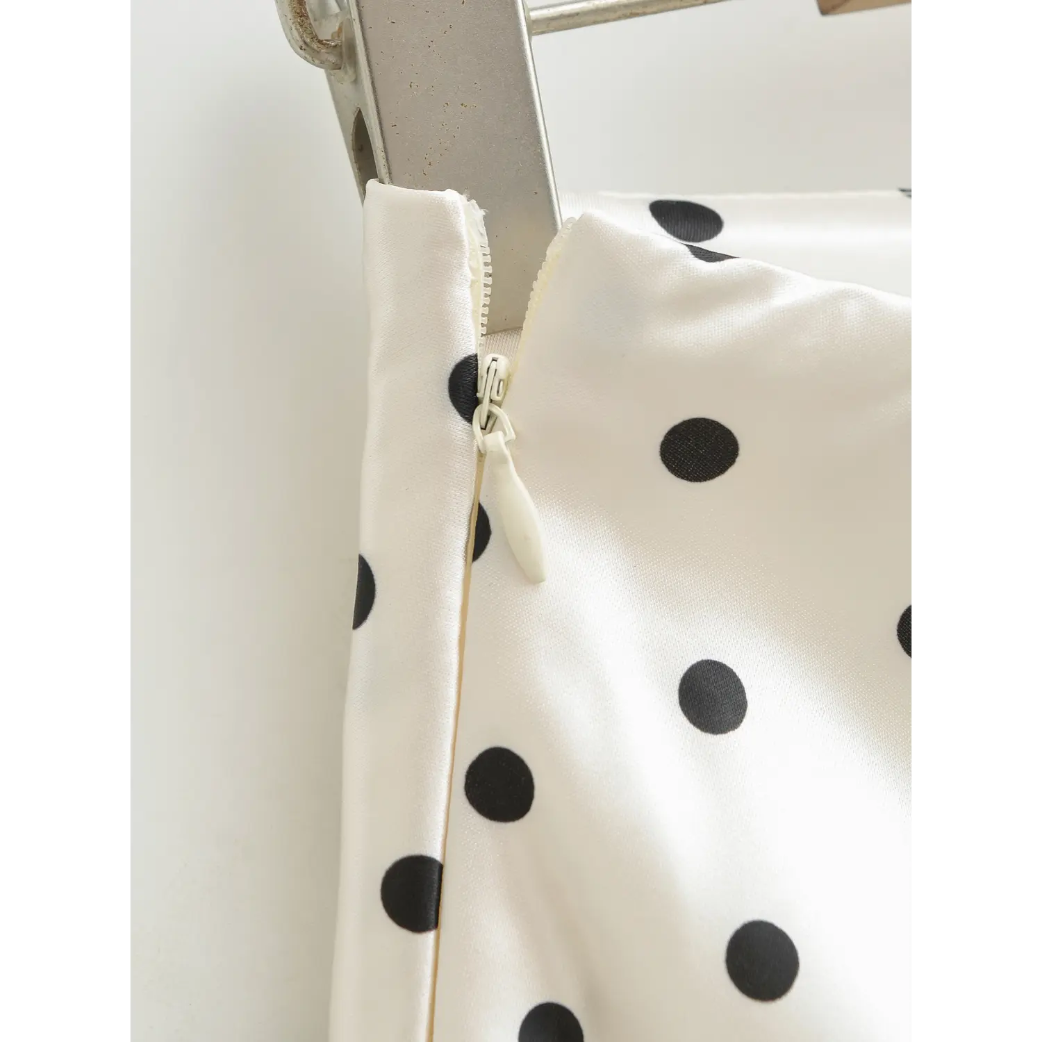 Extreme close-up of invisible hidden side zipper on white polka dot silky satin mini skirt