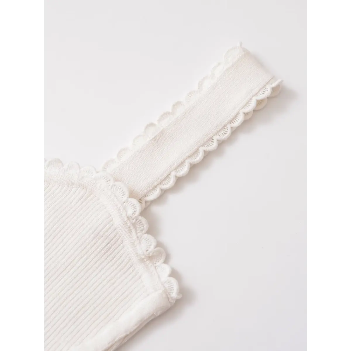 Close-up of the scalloped lace-trimmed strap on a white ribbed cami top, highlighting the delicate knit edge.