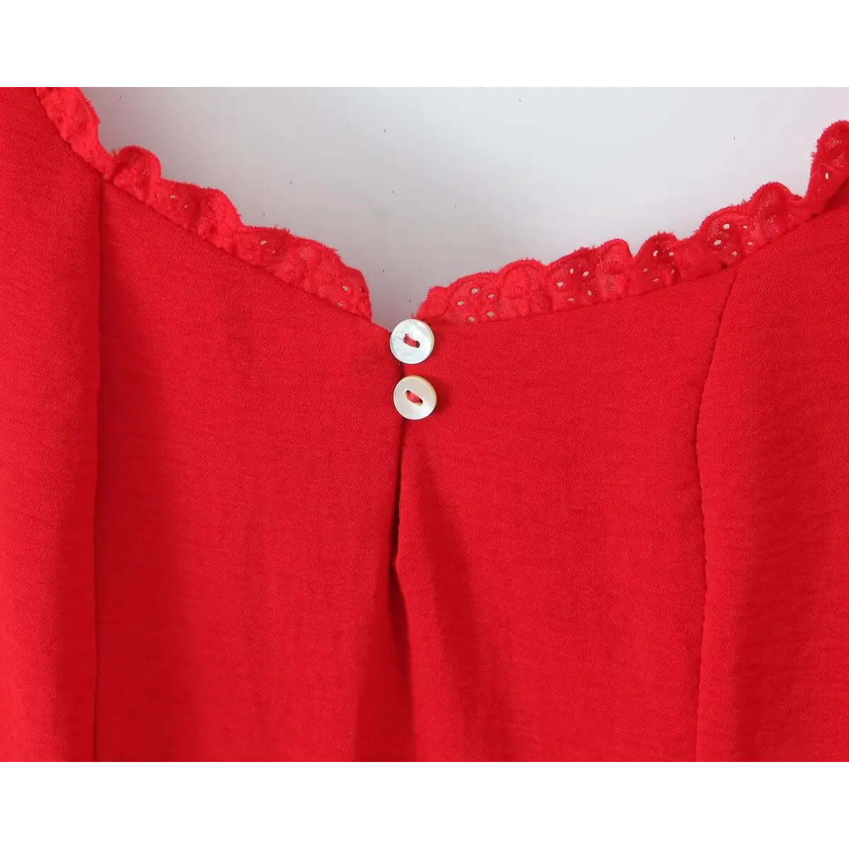 Close-up of the shell buttons on a red lace-trimmed cami dress, showing the mother-of-pearl finish and scalloped lace trim.