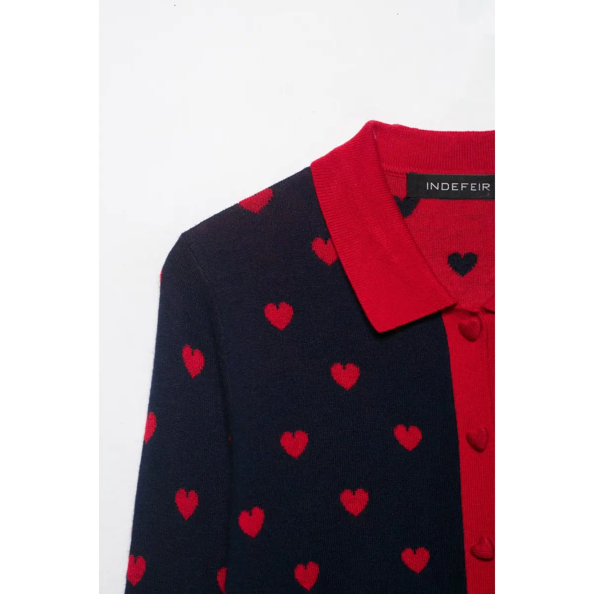 Close-up of the shoulder area of a navy and red heart-patterned knit cardigan, showing the red collar and heart pattern.