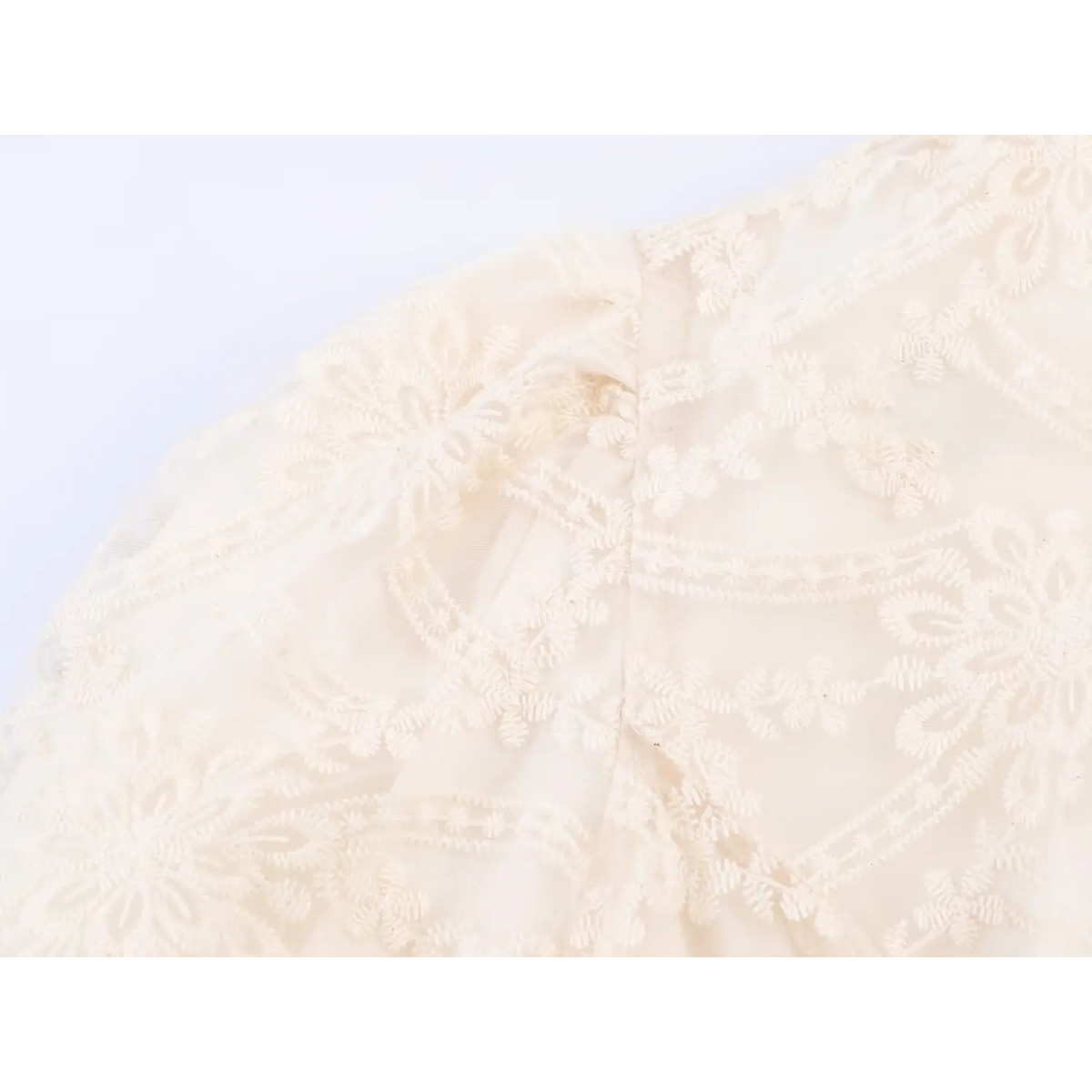 Close-up of shoulder puff seam and floral lace embroidery on beige mini dress