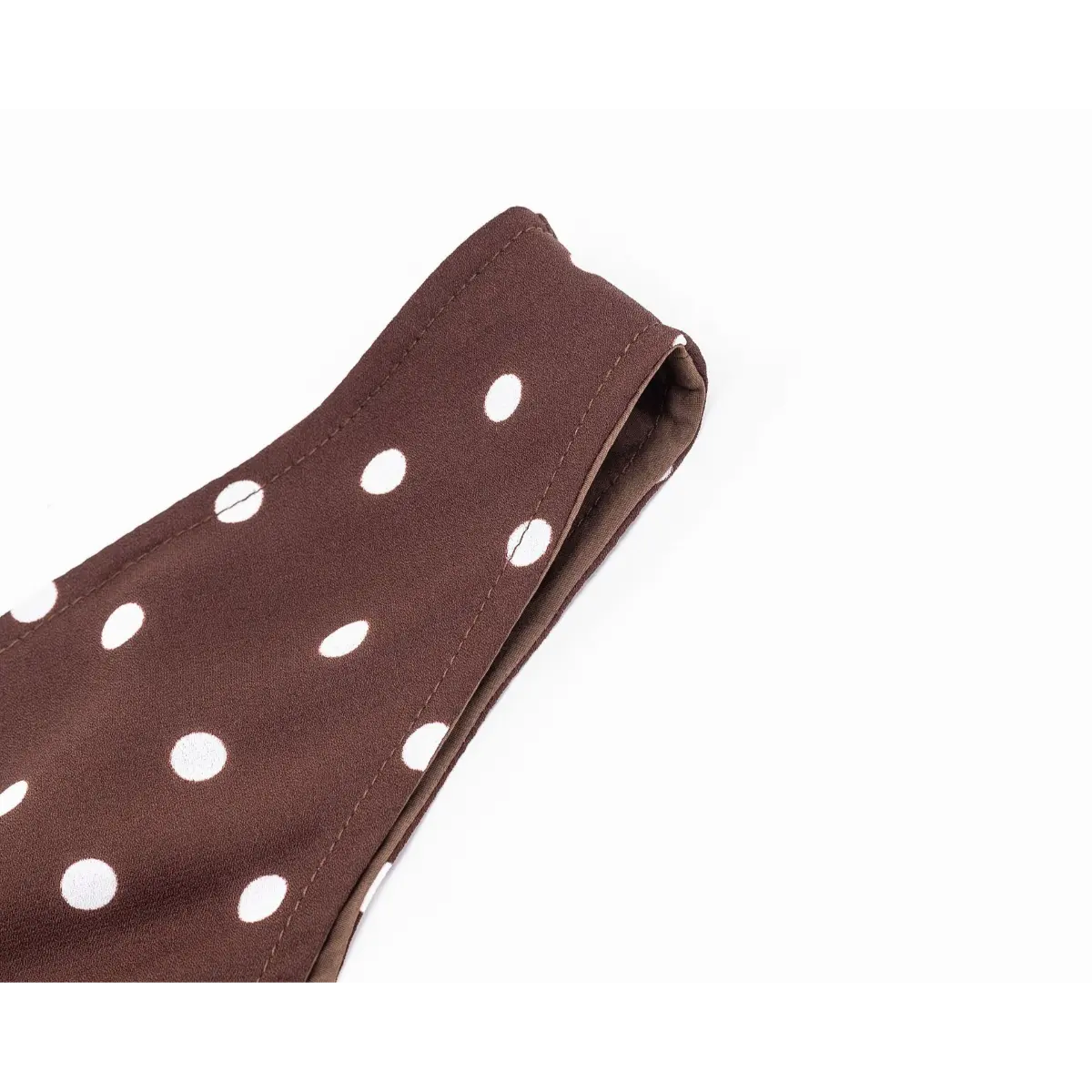 Close-up of the shoulder strap on a brown and white polka dot dress, showing the finished edge and double stitching.