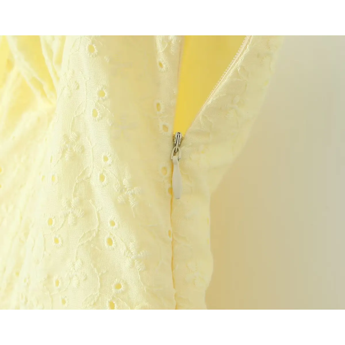 Side seam invisible zipper close-up, matching pale yellow tape zipper on hollow embroidery cotton fabric.