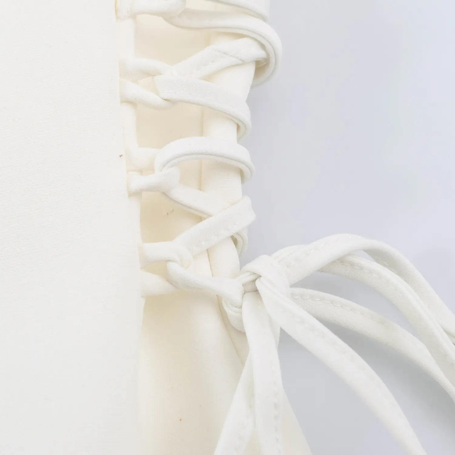 Macro closeup of adjustable side lace-up ribbon ties on white halter mini dress
