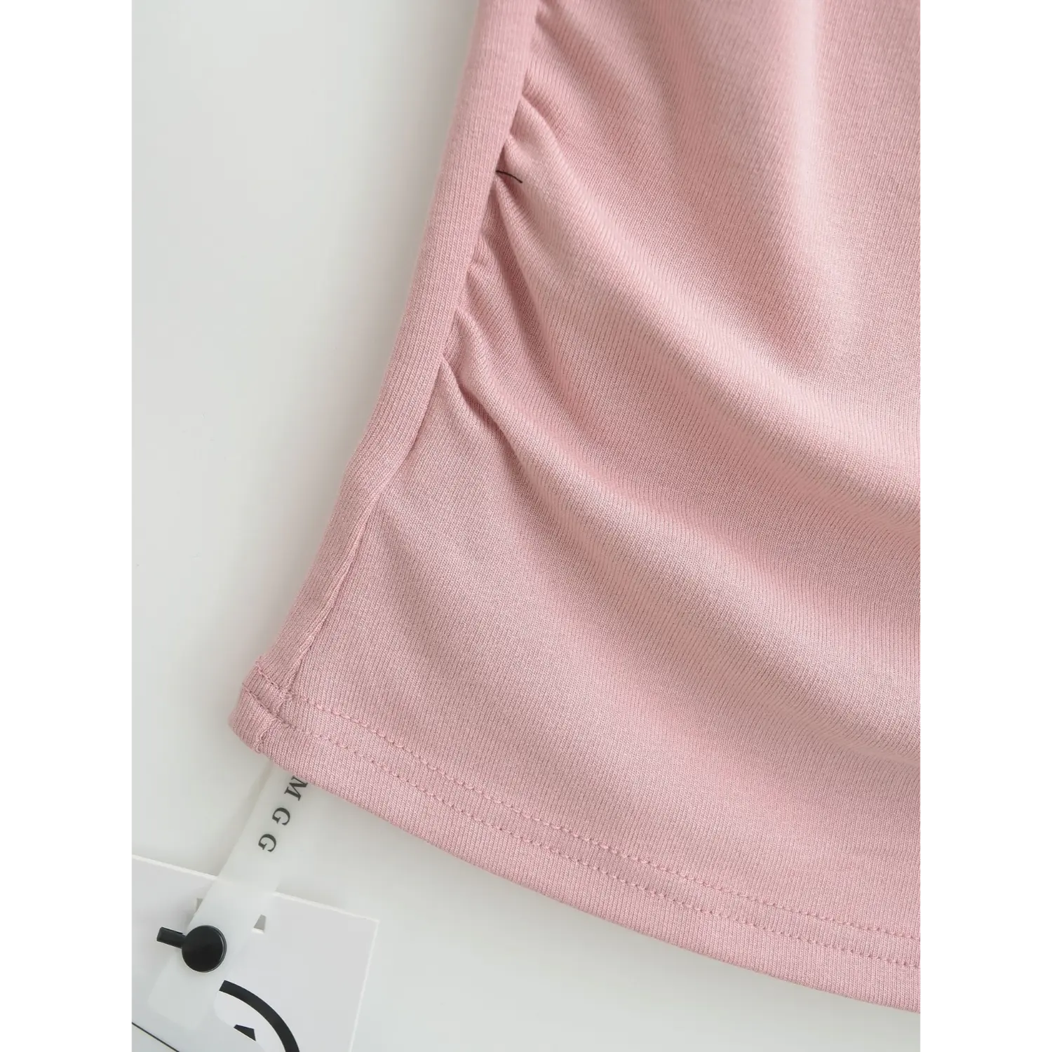 Close-up stitching detail of side waist ruching and bottom hem on dusty pink square neck ribbed cami with brand tag