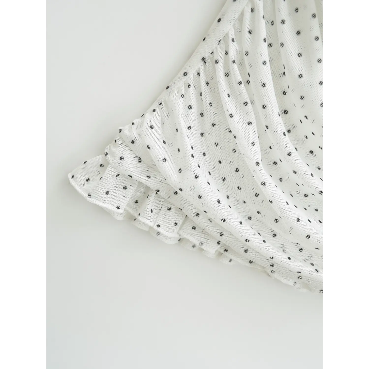 Fabric detail showing vertical side ruching shaping and layered ruffle peplum hem on polka dot mesh casual top