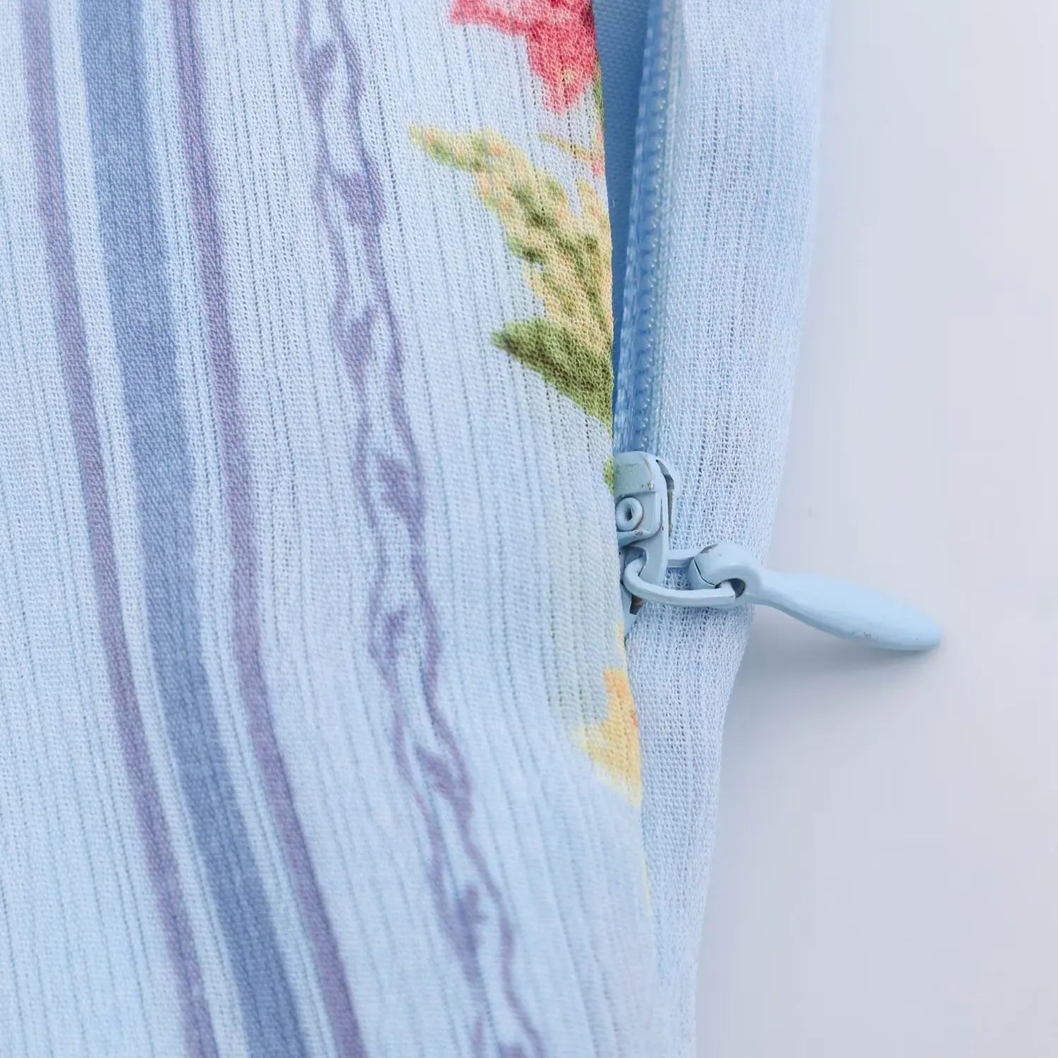Side waist invisible zipper partial shot, light blue zipper pull tab, floral printed fabric tape covered zipper teeth