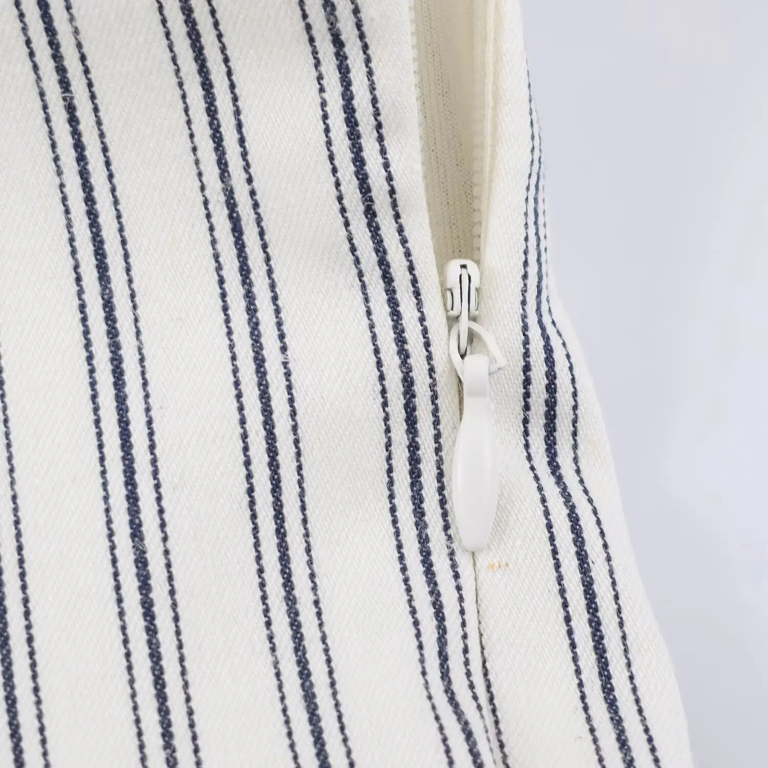 Side waist invisible zipper partial close-up, white zipper pull tab, stripe fabric tape covering zipper teeth