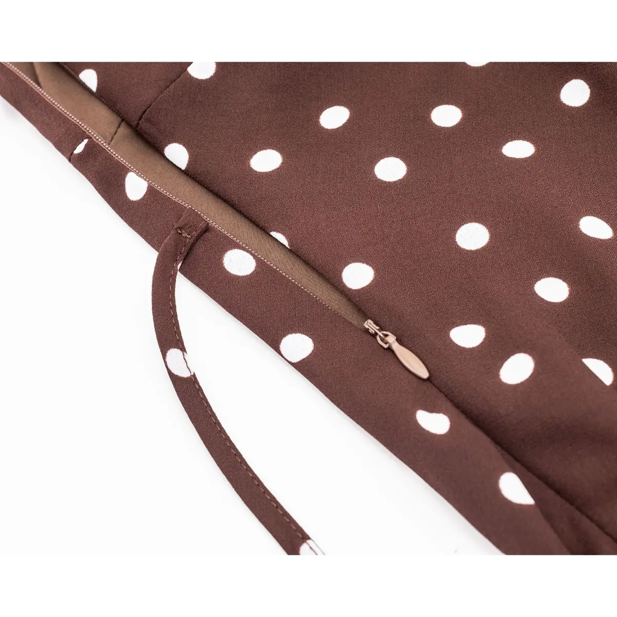 Close-up of the side zipper on a brown and white polka dot dress, highlighting the hidden zipper pull and seam construction.