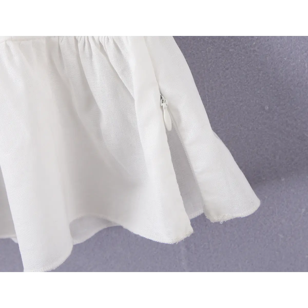  Close-up of the side zipper on a white off-shoulder peplum top, showing the hidden zipper pull and finished seam.
