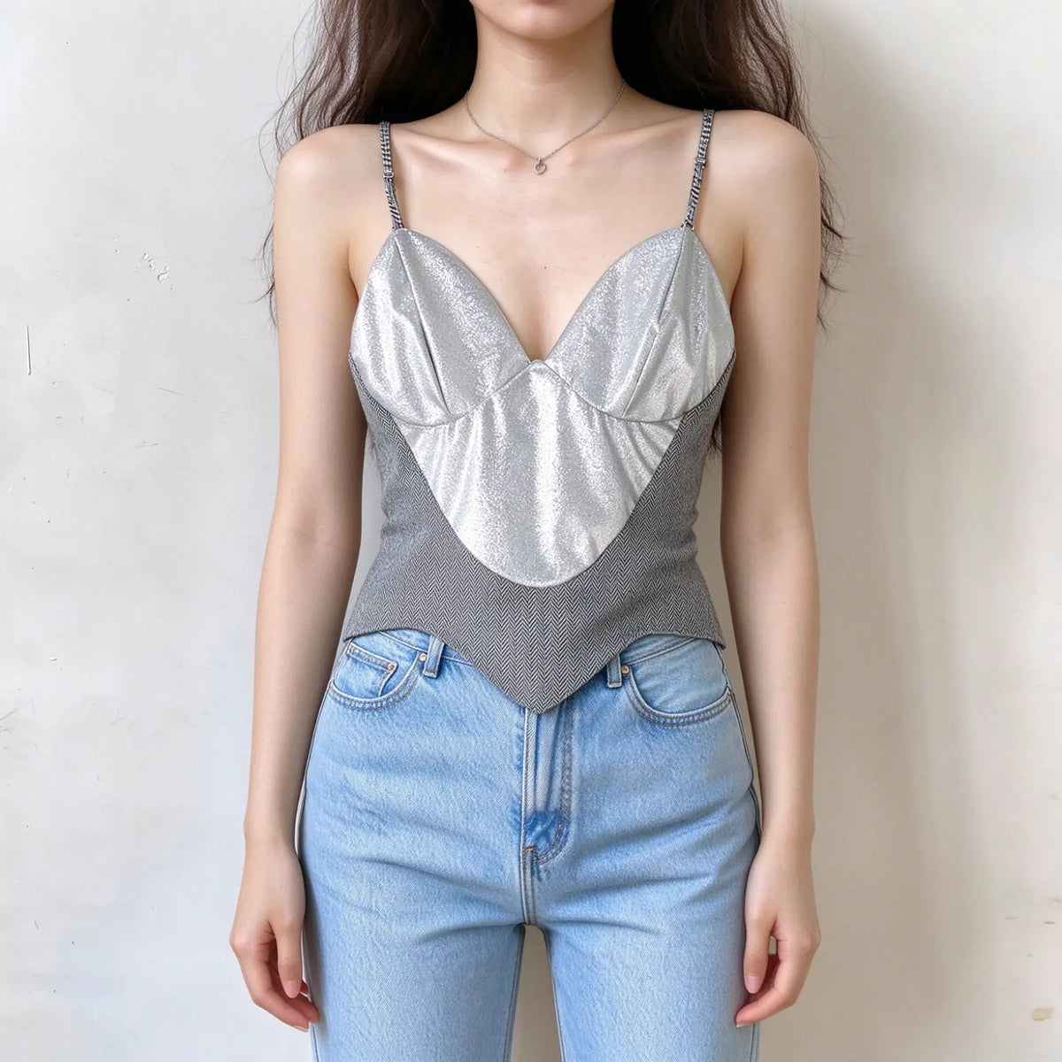 Model wearing silver metallic cami crop top, v neck, zigzag woven hem, rhinestone spaghetti straps, paired with light blue jeans against plain white wall