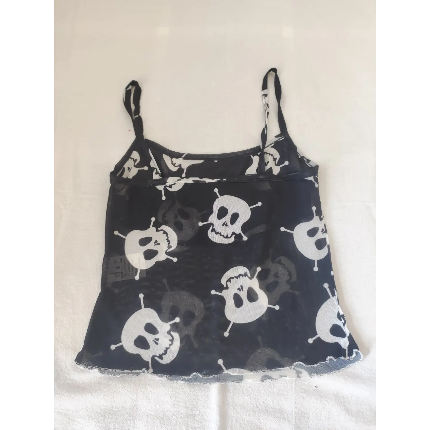 Flat lay back view black sheer mesh crop cami top, white skull allover print, thin spaghetti straps, wavy lettuce hem