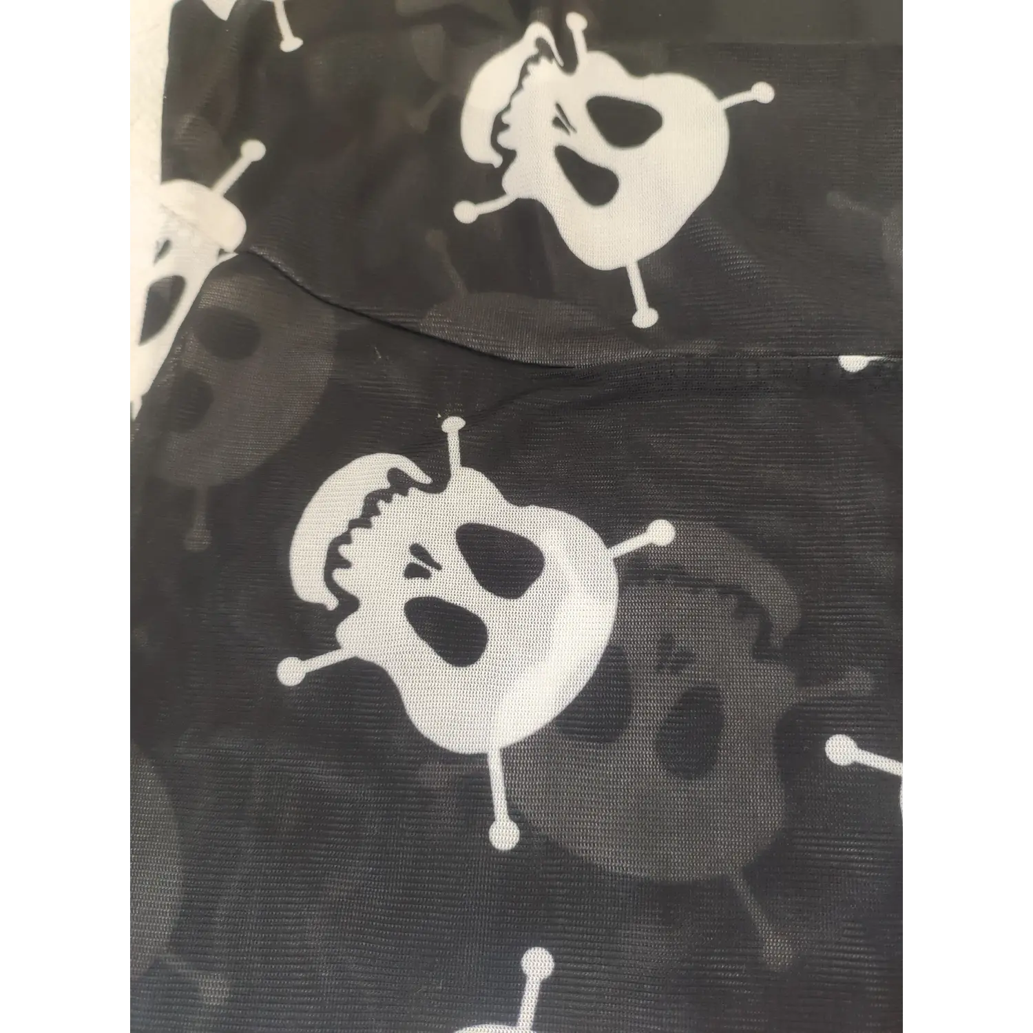 Close-up texture shot of white skull graphic print on black stretch sheer mesh fabric, goth tank top material detail