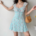 Model wearing skyblue rose floral camisole mini dress with ruffle neckline and front tie