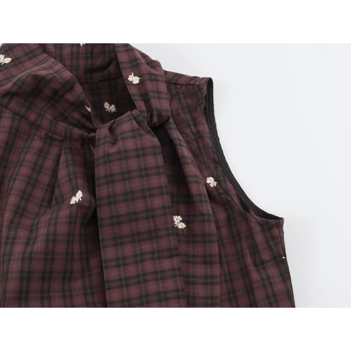 Close-up of pleated collar and black binding edge on plaid vest with white floral embroidery