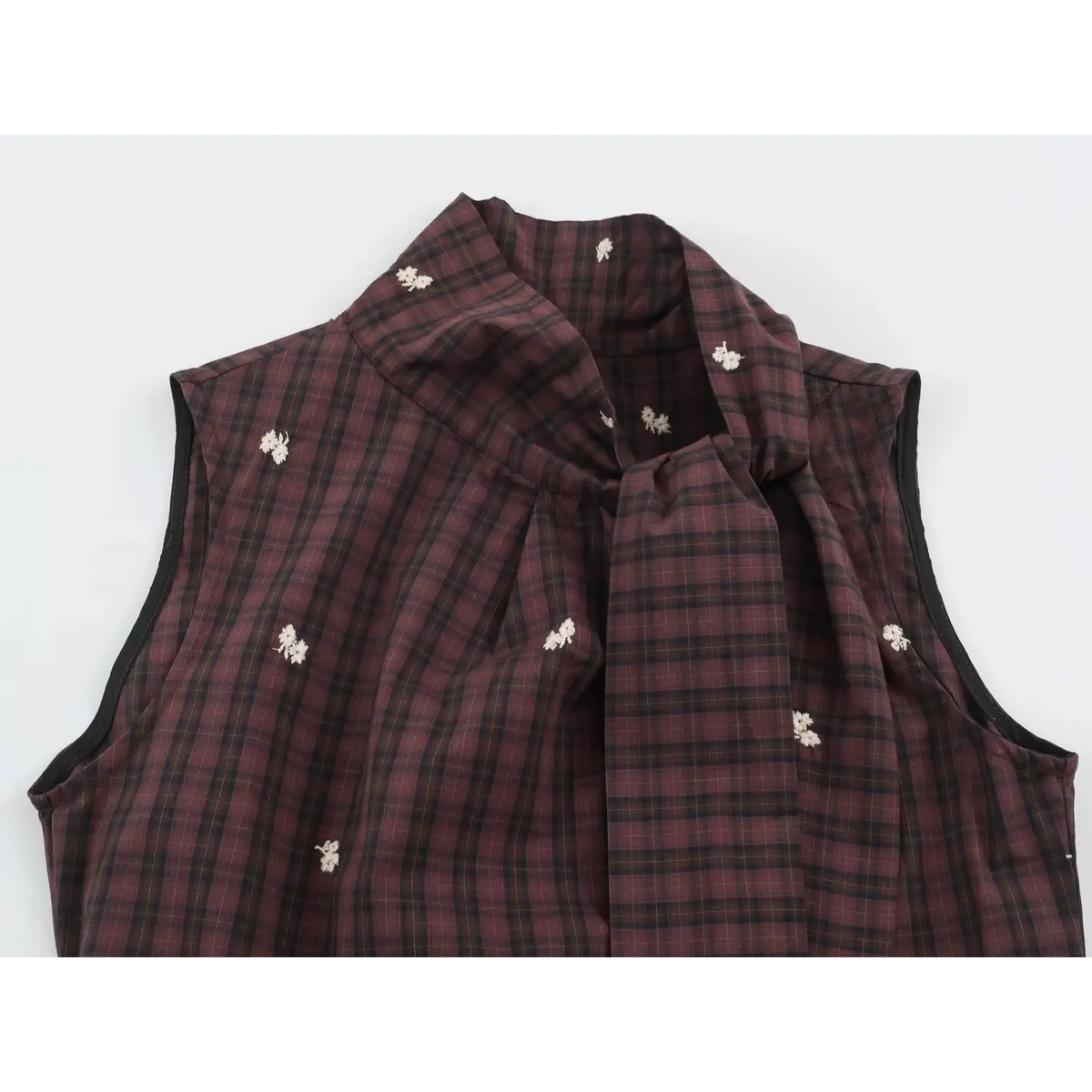 Close-up of stand collar with flowing tie and black bound armhole edge on plaid vest