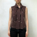 Model wearing sleeveless plaid vest with tie front and floral embroidery, paired with black slim trousers on white background