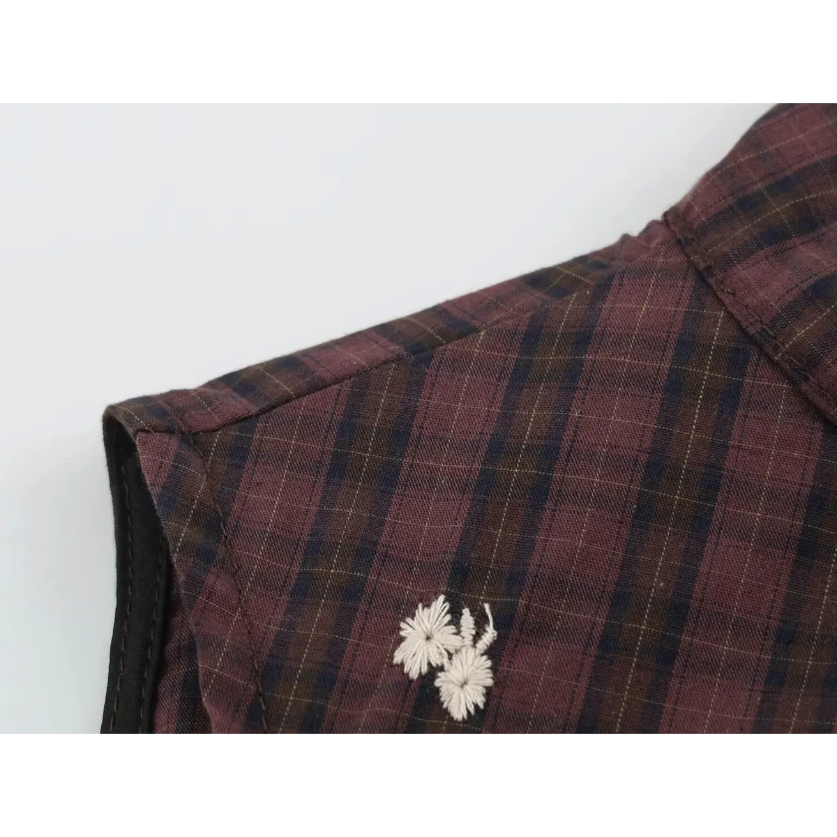 Close-up of shoulder and collar seam on wine red plaid vest with fine yellow check lines, black binding and white floral embroidery