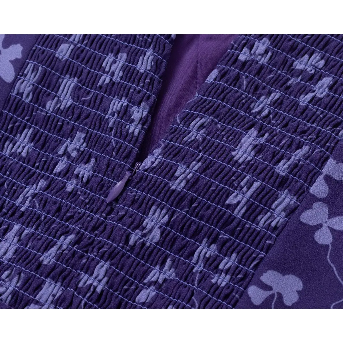Close-up of the smocked back panel and hidden zipper on a purple floral print dress, showing the stretchy texture and zipper pull.