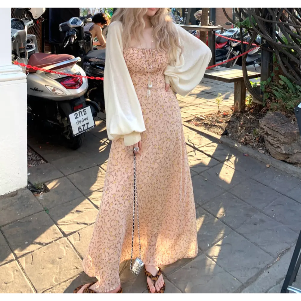 Outdoor street lifestyle shot of pale apricot tiny floral slip maxi dress, thin adjustable straps, layered oversized cream puff sleeve knit cardigan, styled with leopard print slide sandals and mini silver chain bag