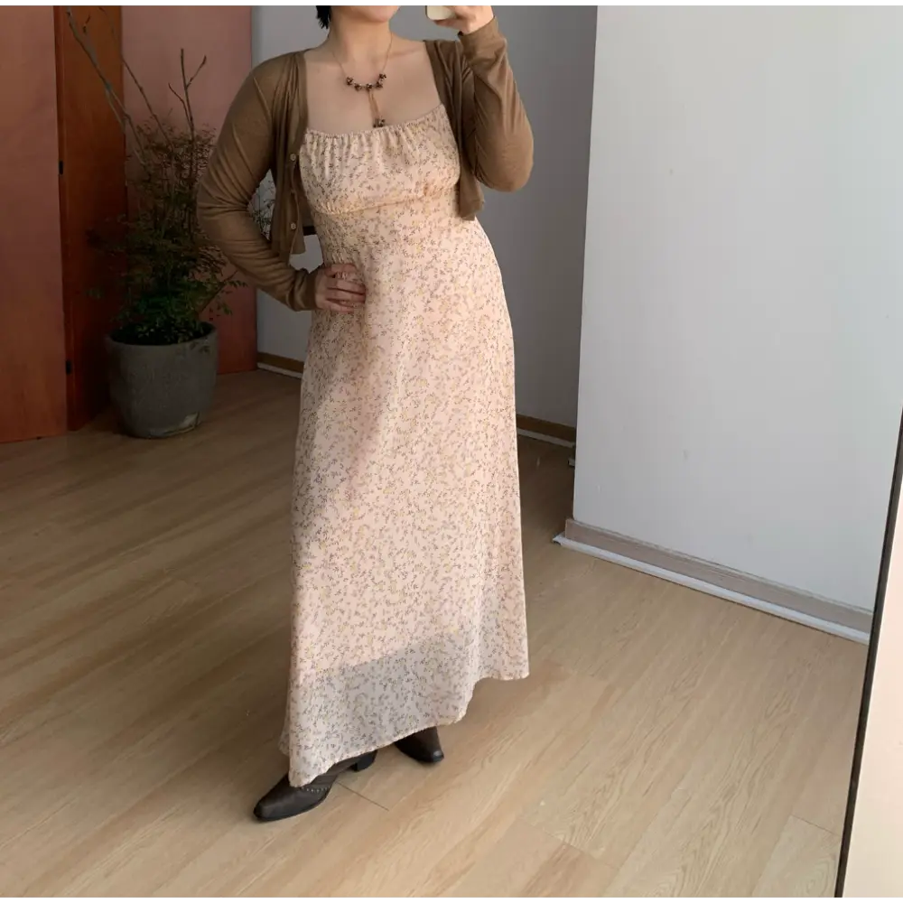 Full body indoor mirror shot of pale peach ditsy floral maxi slip dress, layered slim brown long sleeve cropped knit cardigan, matching dark brown pointed leather ankle boots