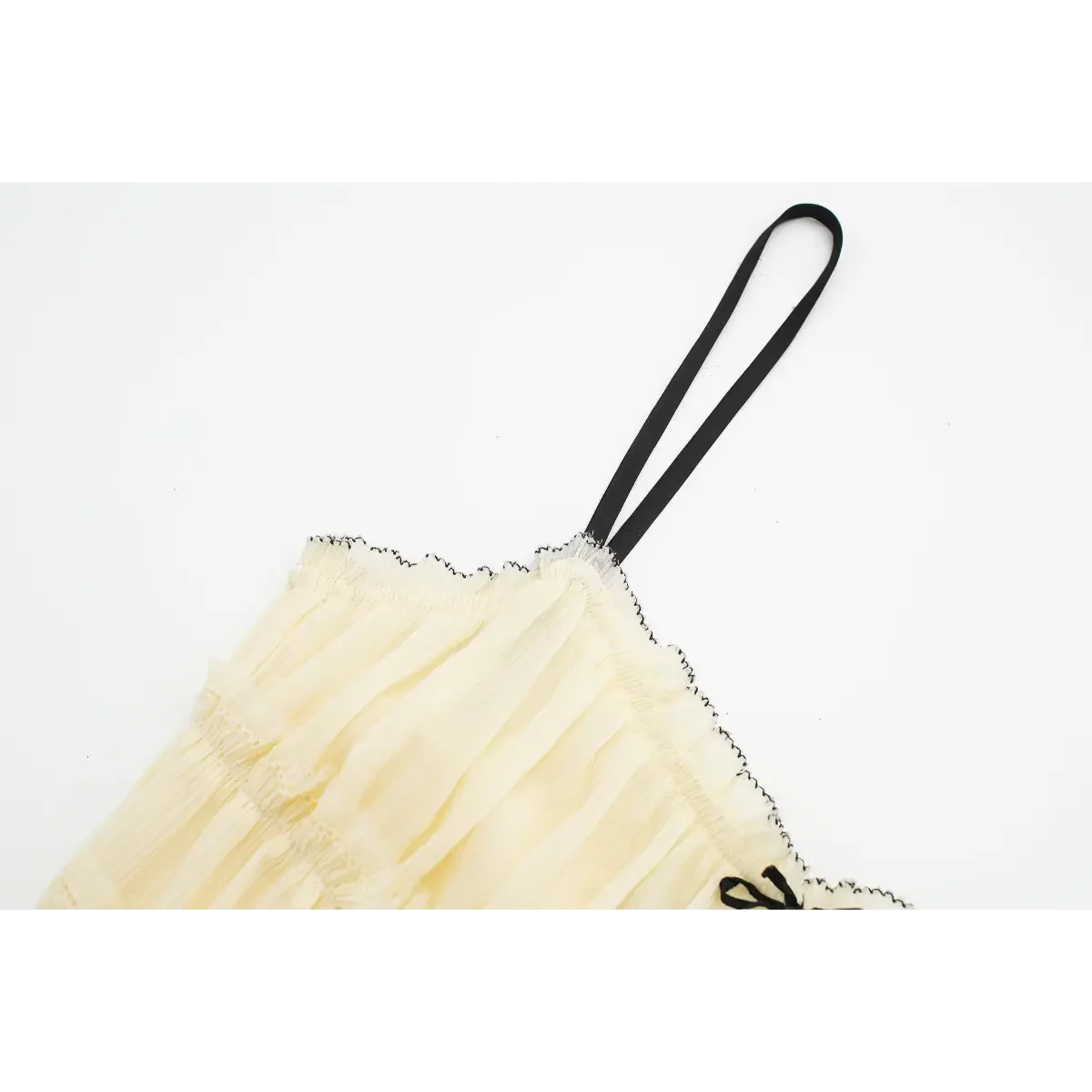 Close-up of the black spaghetti strap on a cream smocked cami dress, showing its attachment to the contrast-trimmed neckline.