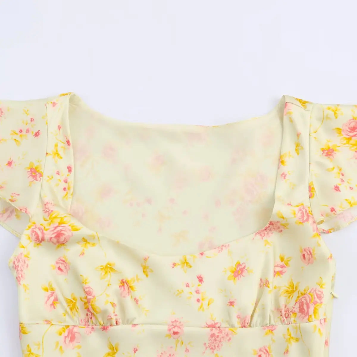 Close-up of the square neckline and gathered bodice on a pale yellow floral dress, highlighting the floral print.