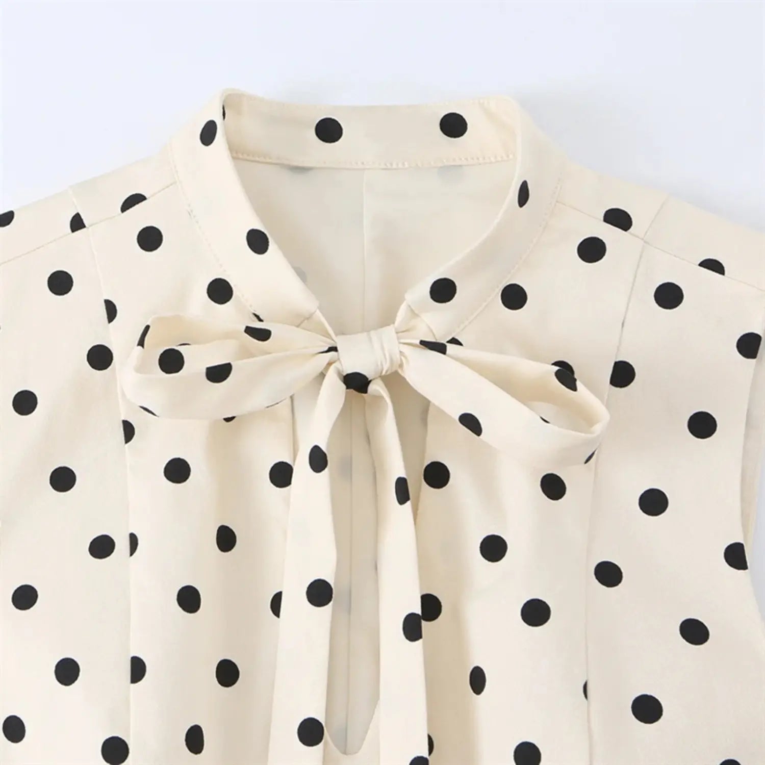 Upper neck partial close-up, small stand collar, front self-fabric tie bow, V hollow cutout, smooth matte woven fabric with black polka dots