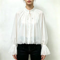 Model wearing white stand collar tie neck lace trim bell sleeve blouse with black trousers