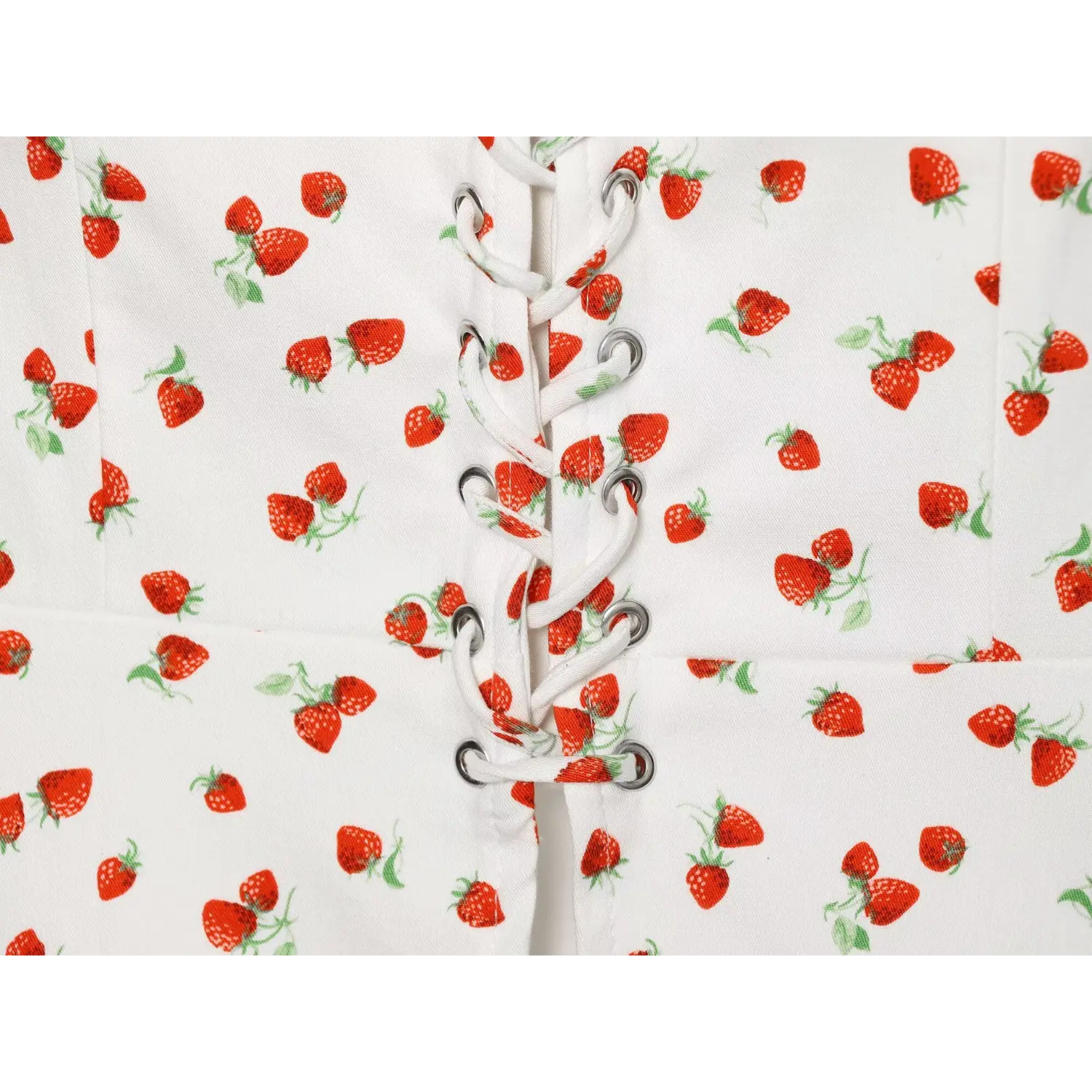 Macro close‑up of metal eyelets and white lace‑up cord on strawberry print cami top