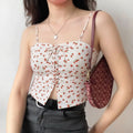 Model wearing front view white lace‑up cami top with all‑over red strawberry print paired with denim bottoms