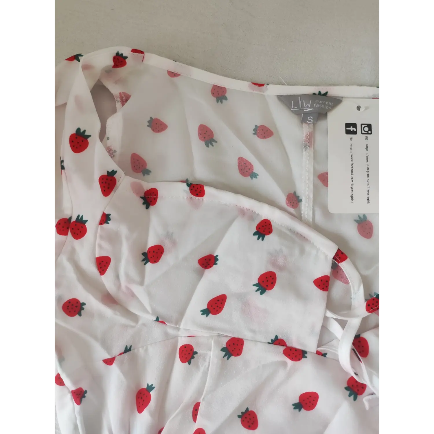Close-up shot of white crop top with red strawberry print, brand label and hang tag