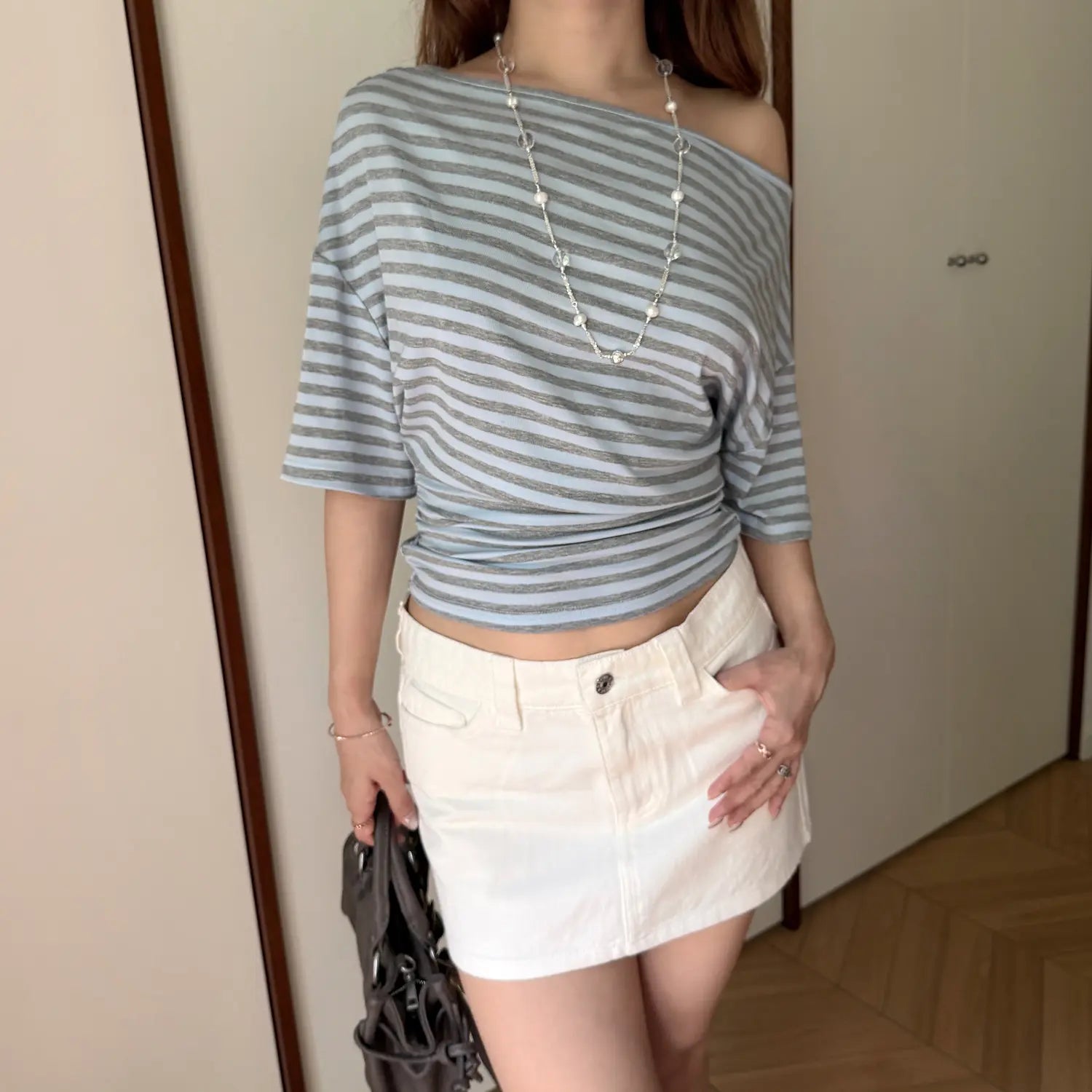 Full body lifestyle shot, model wearing blue grey striped off shoulder top matched with white denim mini skirt