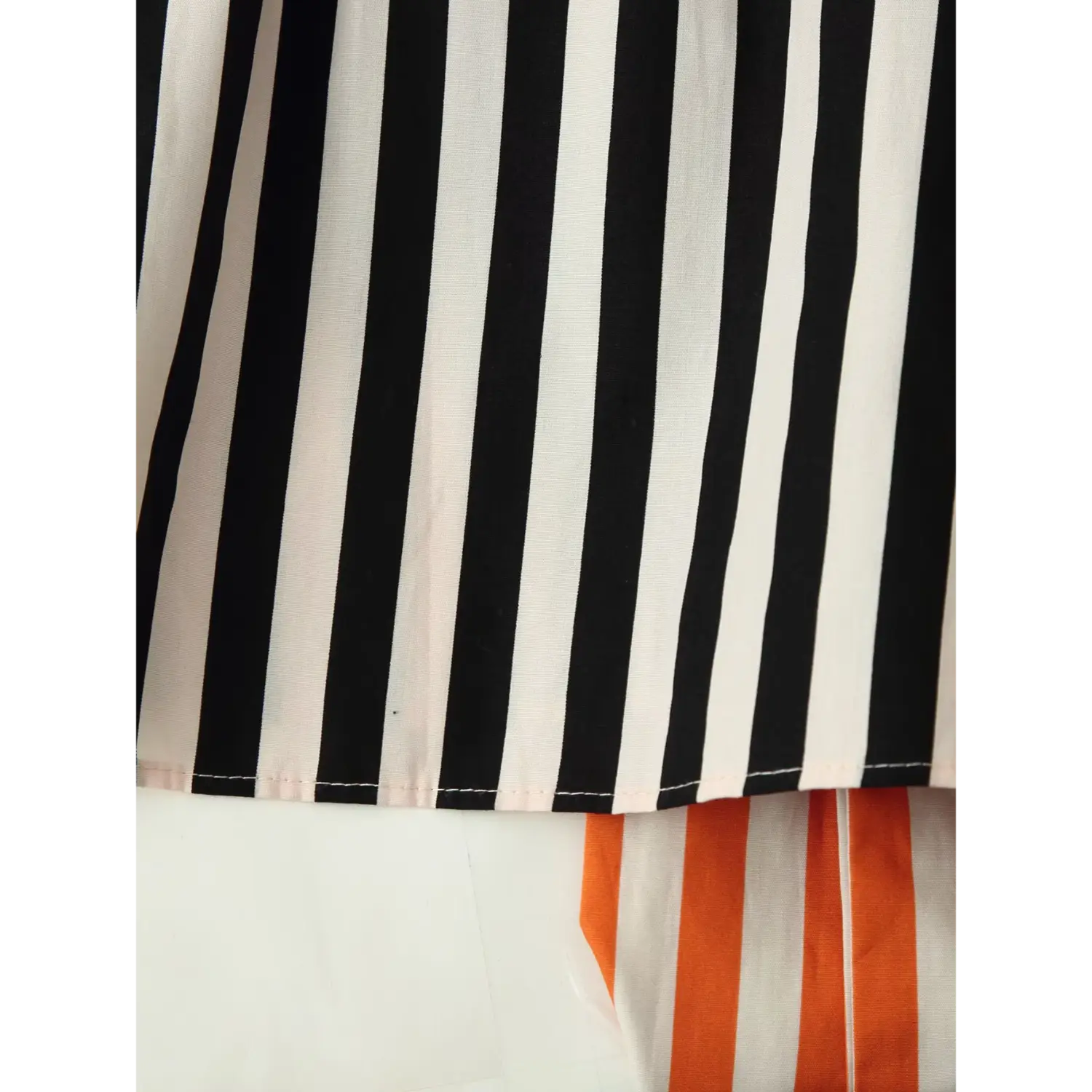 Partial close‑up of shirt bottom hem, black off‑white vertical stripe woven fabric, neat finished hem stitching, partial sash corner