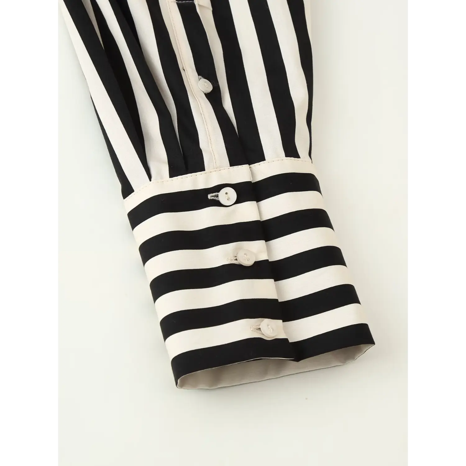 Close‑up view of striped shirt cuff with multiple shell buttons, black‑off‑white horizontal stripe cuff detail