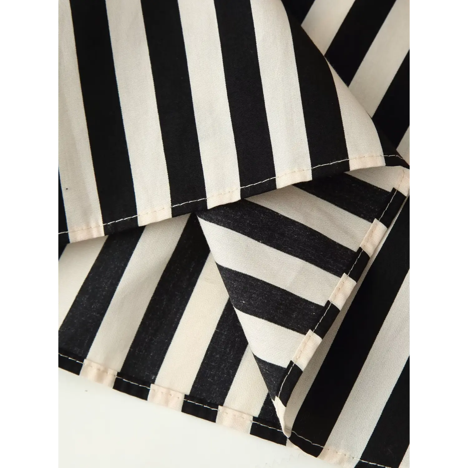 Macro close‑up of folded shirt hem, double‑stitch finish, black‑off‑white vertical stripe fabric inner layer view