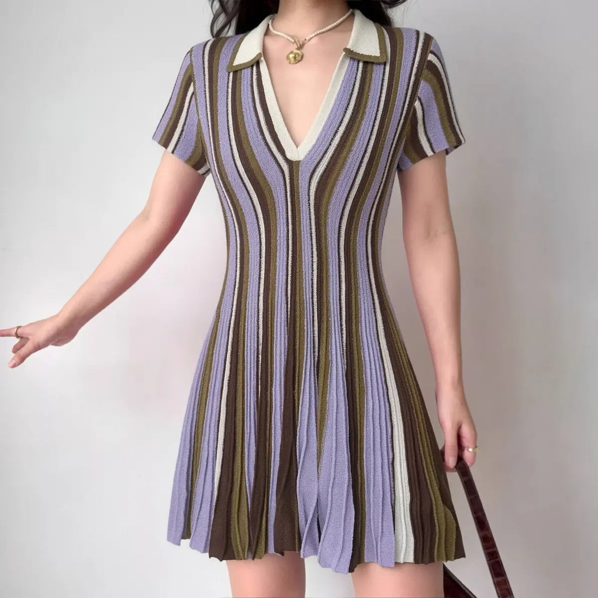 The striped knit mini dress worn by a model, showing the fitted silhouette, pleated skirt, and color palette