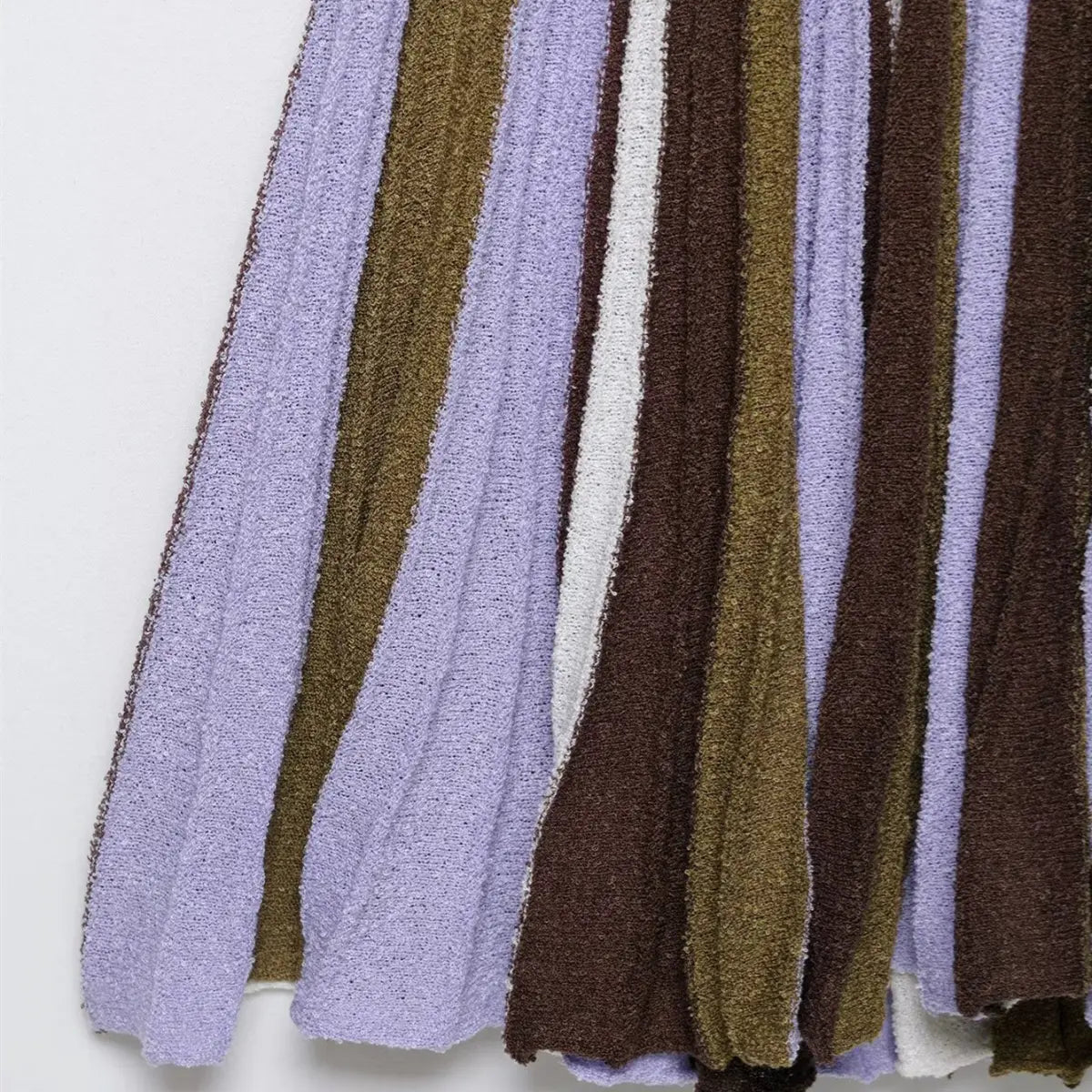 Close-up of the pleated skirt hem on the striped knit mini dress, showing the vertical stripe pattern in lavender, brown, olive, and white