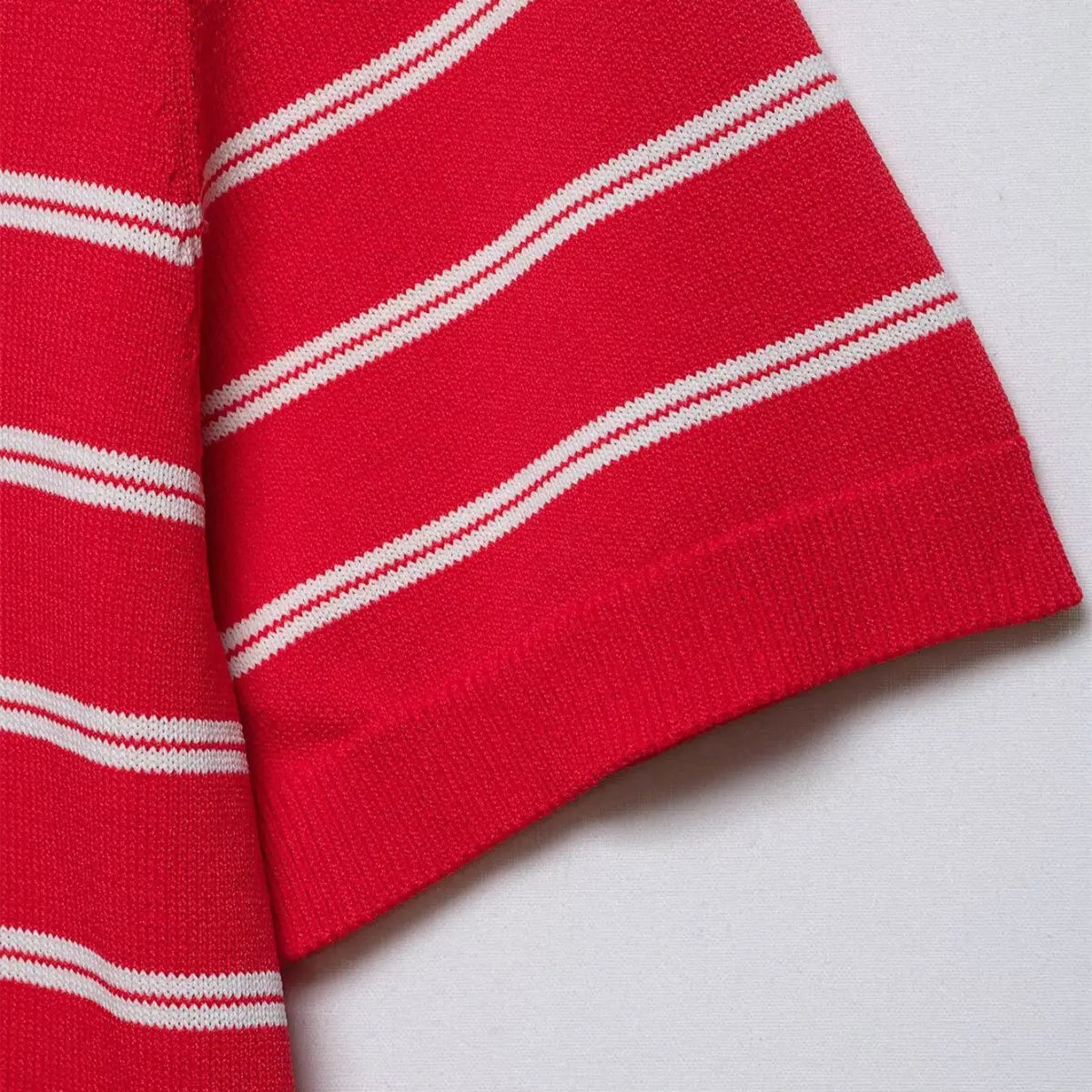 Close-up of the sleeve cuff on the red and white striped knit polo shirt, showing the ribbed finish and double stripe pattern