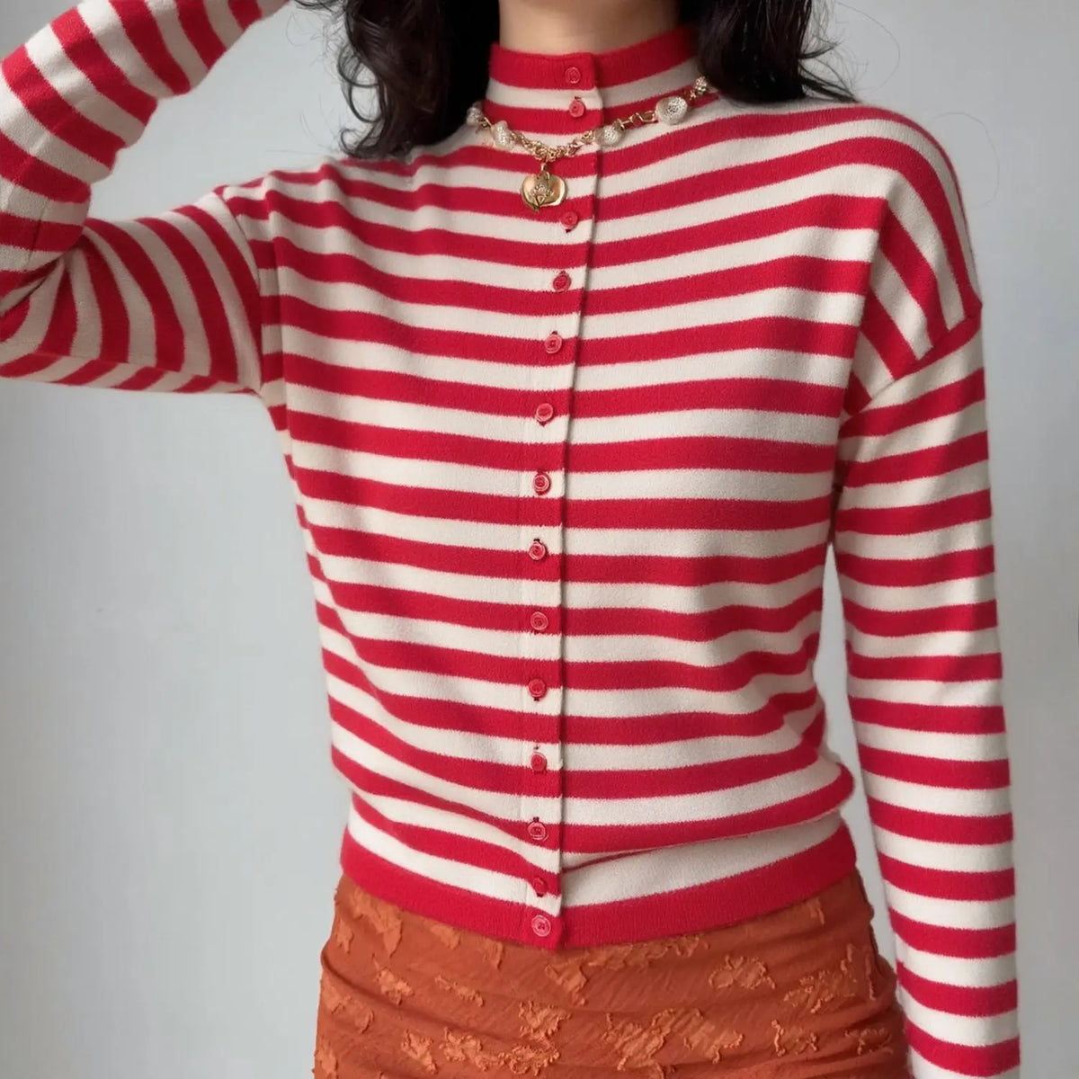 Model wearing red and cream striped knit cardigan with pearl necklace