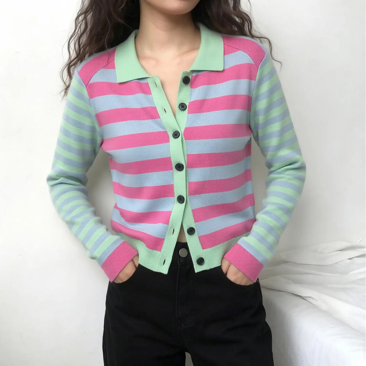 Model wearing pink blue striped knit cardigan with black pants on white background