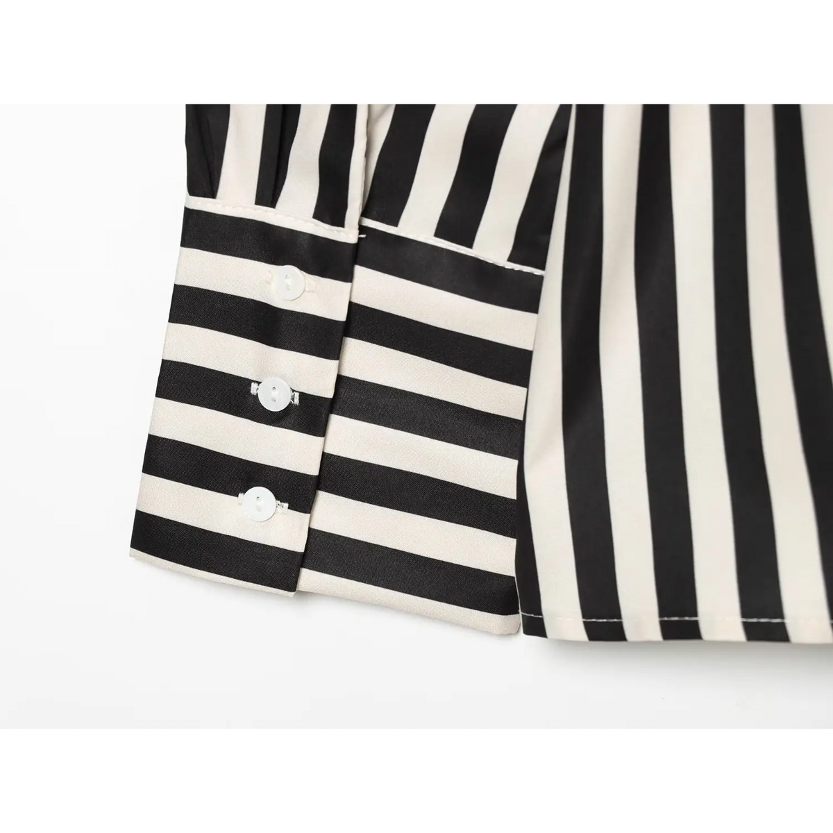 Close‑up of long sleeve cuff with white shell buttons, horizontal black‑cream contrast striped cuff
