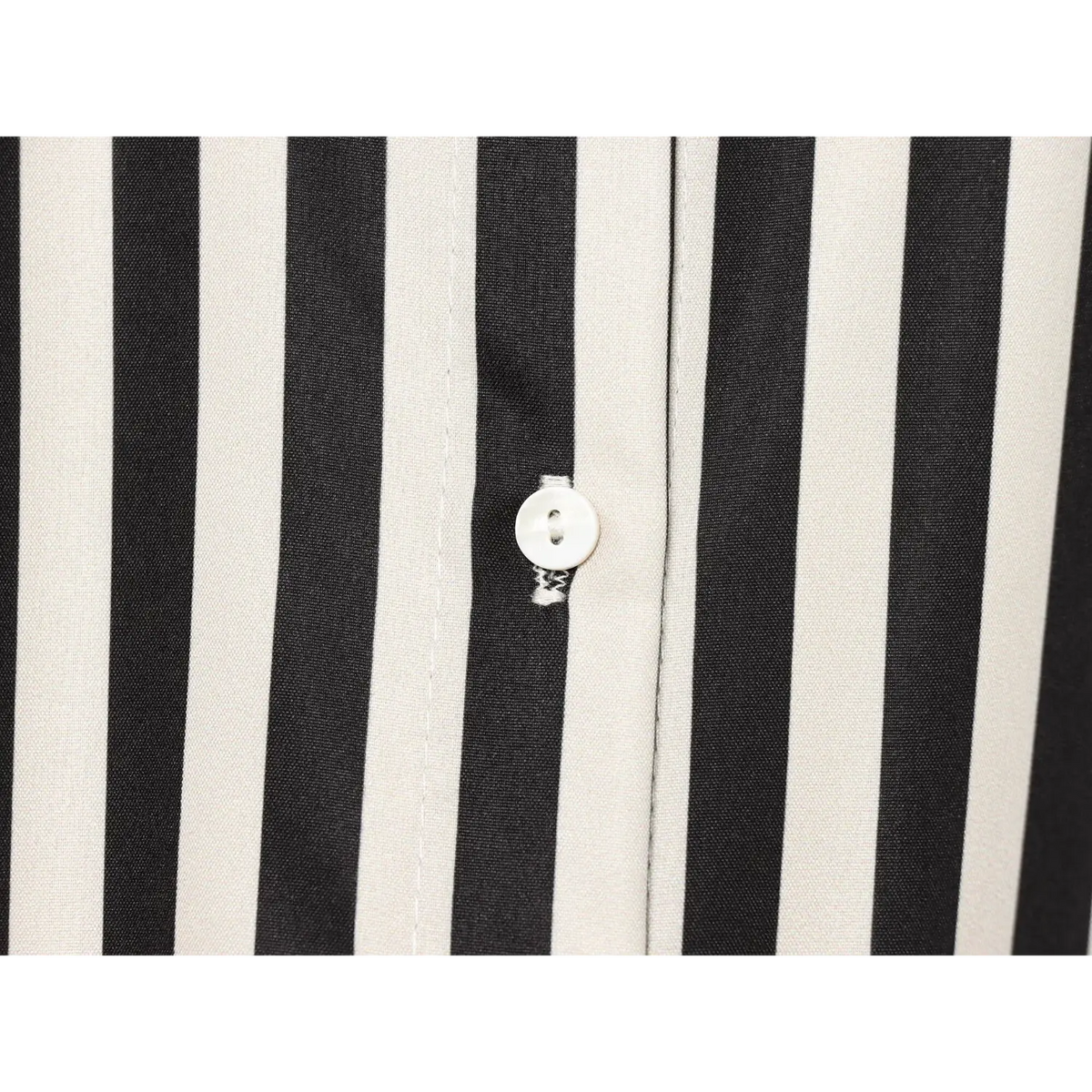 Macro close‑up of white round shell button on vertical black‑cream striped shirt placket
